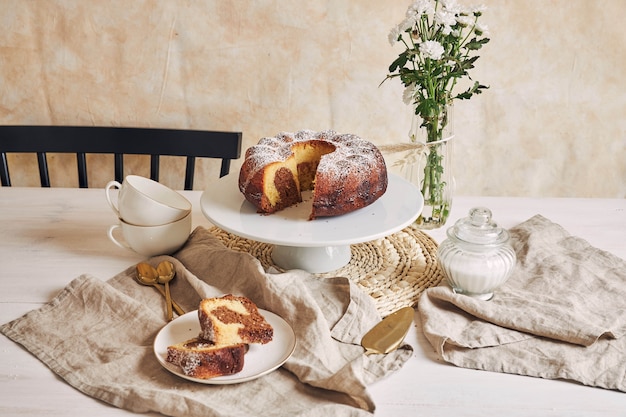 Hermosa foto de un delicioso pastel de anillo puesto en un plato blanco y una flor blanca cerca