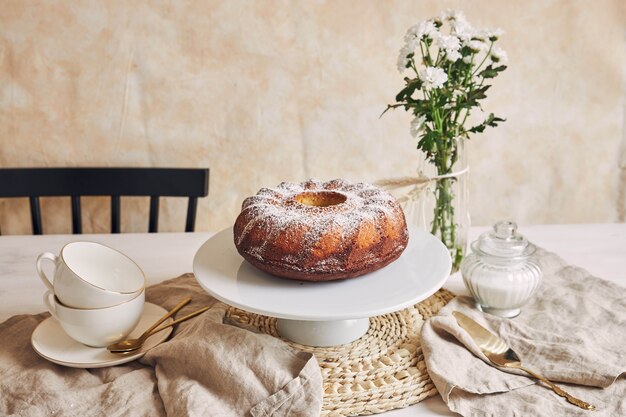 Hermosa foto de un delicioso pastel de anillo puesto en un plato blanco y una flor blanca cerca