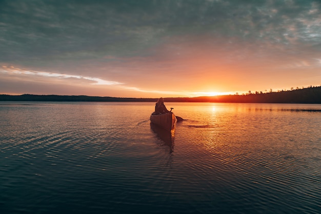 Hermosa foto distante de una mujer montando kayak en medio de un lago durante el atardecer