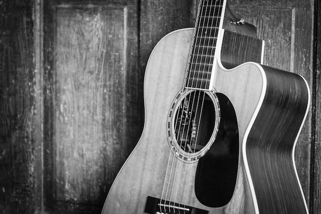 Hermosa foto en escala de grises de una guitarra acústica apoyada en una puerta de madera sobre una superficie de madera