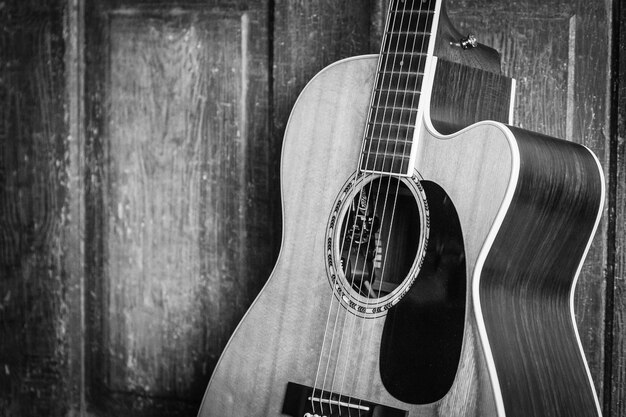 Hermosa foto en escala de grises de una guitarra acústica apoyada en una puerta de madera sobre una superficie de madera