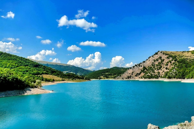 Hermosa foto de un estanque rodeado de montañas bajo un cielo azul en Umbría, Italia