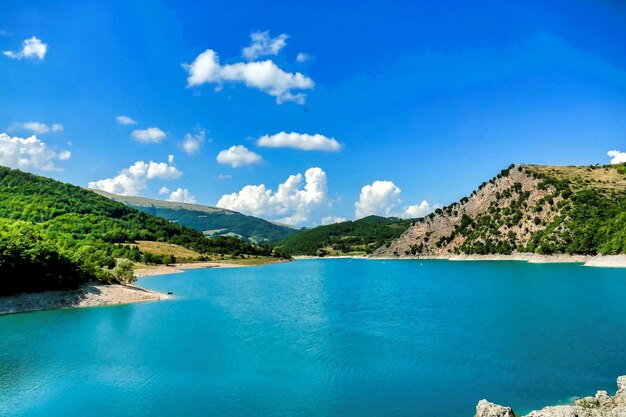 Hermosa foto de un estanque rodeado de montañas bajo un cielo azul en Umbría, Italia
