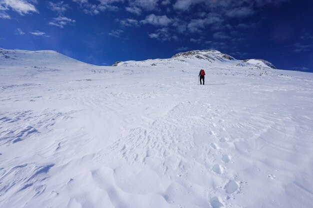 Hermosa foto de un excursionista con una mochila de viaje roja subiendo una montaña bajo el cielo azul