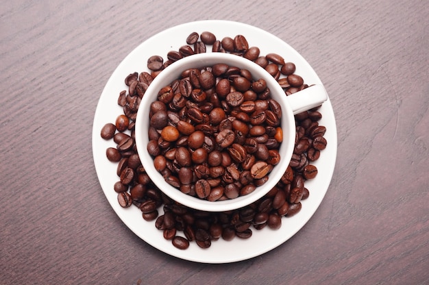 Hermosa foto de granos de café en la taza blanca y el plato sobre una mesa de madera