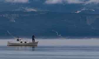 Foto gratuita hermosa foto de un hombre en un barco pescando en el lago con montañas al fondo