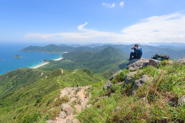 Hermosa foto de un hombre capturando un paisaje de colinas boscosas y un océano azul