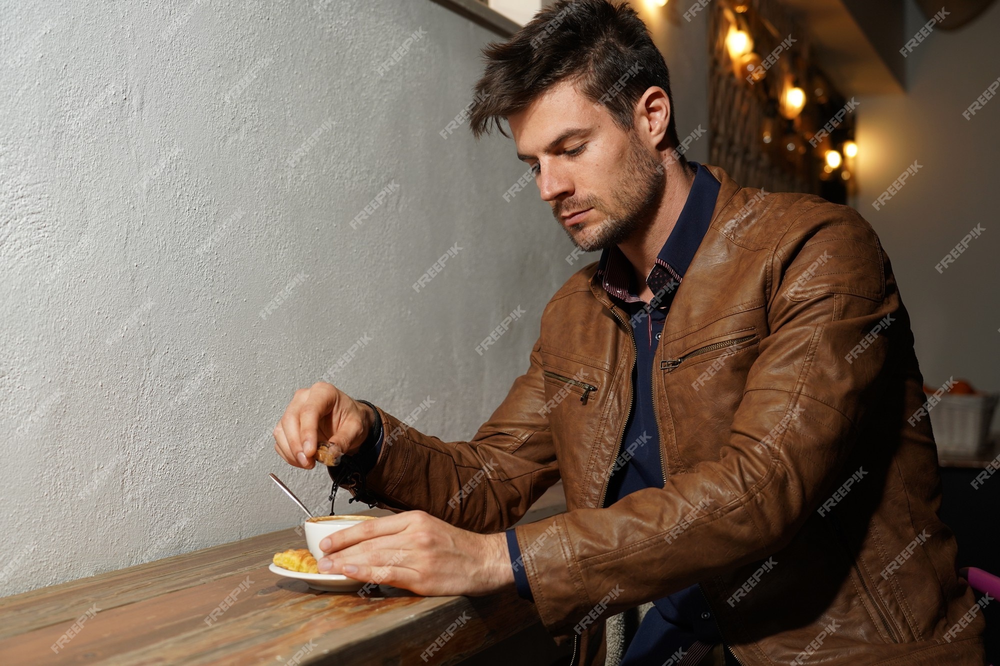Hermosa foto de un hombre elegante una chaqueta de cuero marrón agregando azúcar su café | Foto Gratis