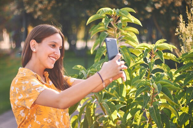 Hermosa foto de una joven con una camisa amarilla tomando un selfie junto a los arbustos