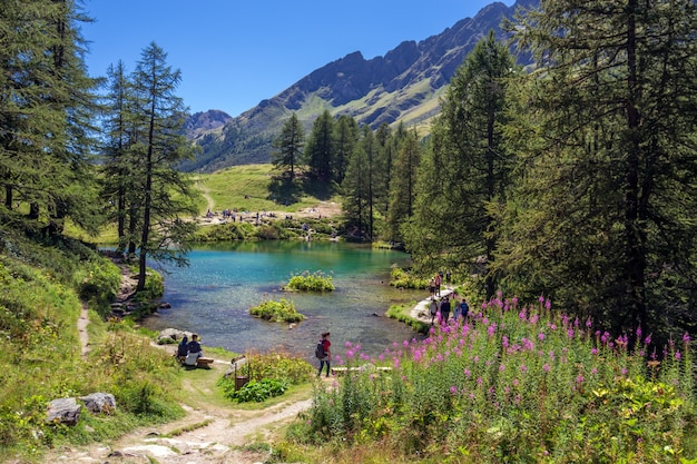 Hermosa foto de un lago cerca de las montañas y rodeado de árboles y personas
