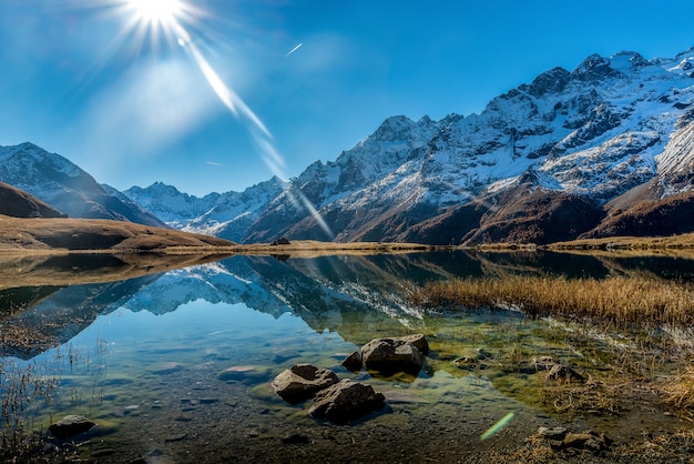 Hermosa foto de un lago cristalino junto a una base de montaña nevada durante un día soleado