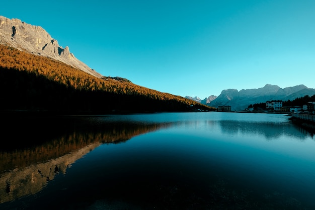 Hermosa foto de un lago en medio de árboles amarillos en la colina y el edificio en una orilla