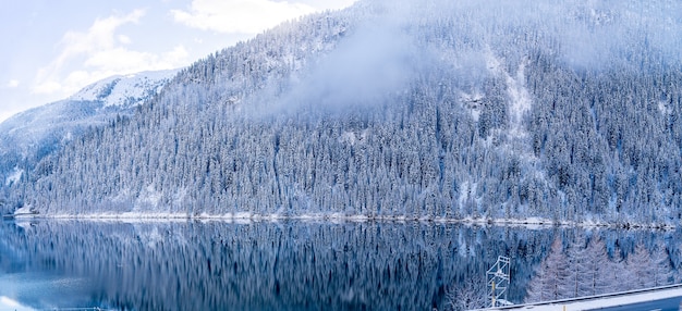 Hermosa foto de un lago tranquilo con montañas boscosas cubiertas de nieve a los lados