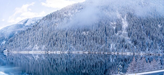 Hermosa foto de un lago tranquilo con montañas boscosas cubiertas de nieve a los lados