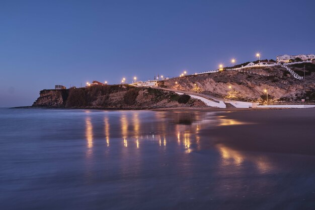 Hermosa foto de luces en una colina rocosa en la playa con un cielo azul claro