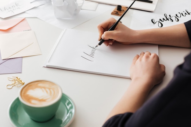 Hermosa foto de manos de mujer sosteniendo un bolígrafo de tinta clásico mientras escribe notas en un escritorio blanco