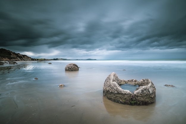 Hermosa foto del mar con rocas y montañas en la distancia bajo un cielo nublado azul