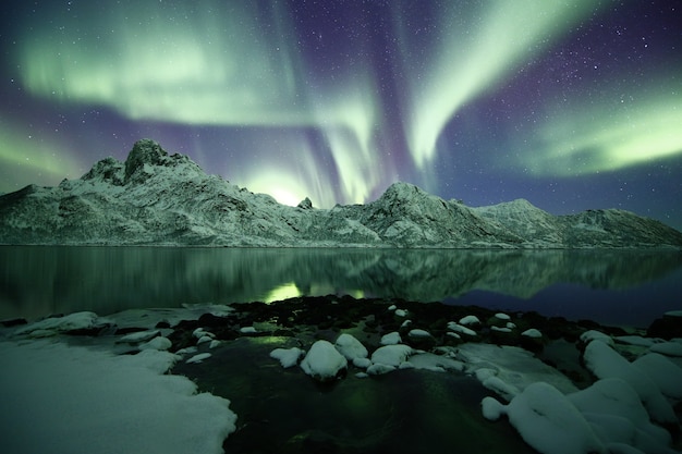 Una hermosa foto de montañas nevadas bajo una luz polar.