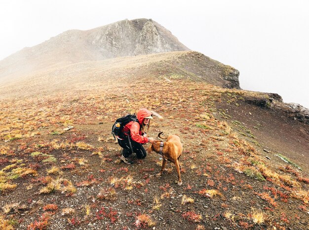 Hermosa foto de una mujer acariciando a un perro en una montaña con un cielo blanco