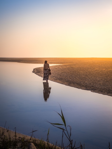 Hermosa foto de una mujer caminando por la playa durante la puesta de sol