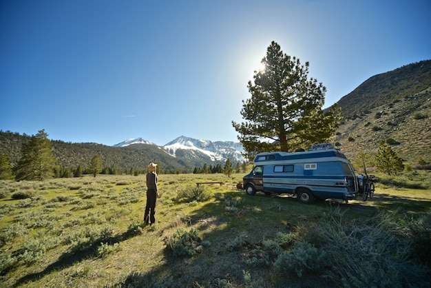 Hermosa foto de una mujer de pie en un campo de hierba cerca de una camioneta con montaña