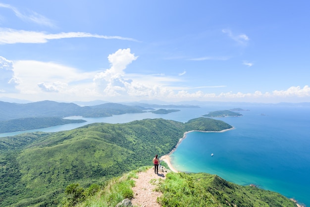 Hermosa foto de una mujer de pie sobre un paisaje de colinas boscosas y un océano azul