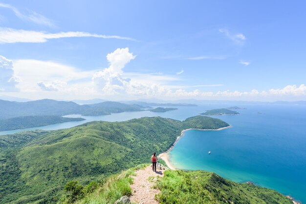 Hermosa foto de una mujer de pie sobre un paisaje de colinas boscosas y un océano azul