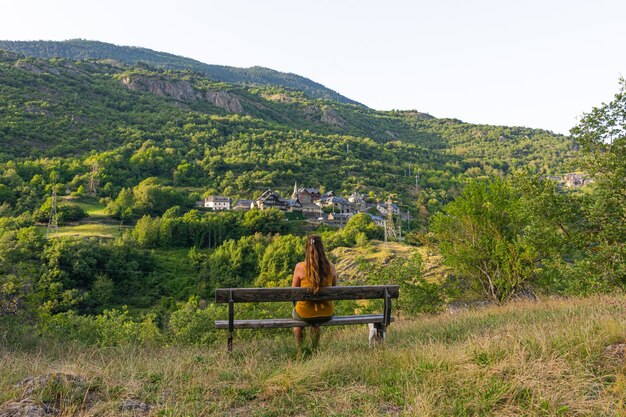 Hermosa foto de una mujer sentada en el banco frente a un paisaje de montaña