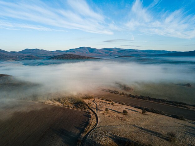 Hermosa foto de una niebla blanca sobre el campo con una carretera y montañas con un cielo azul