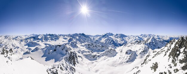 Hermosa foto panorámica de cadenas montañosas cubiertas de nieve bajo un cielo soleado azul claro