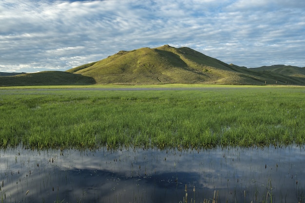 Hermosa foto de pantano de agua dulce con una montaña verde y un cielo azul nublado en el