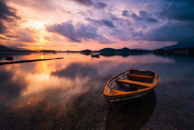 Hermosa foto de un pequeño lago con un bote de remos de madera en foco y nubes impresionantes en el cielo