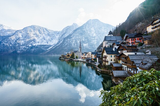 Hermosa foto de un pequeño pueblo rodeado por un lago y colinas nevadas