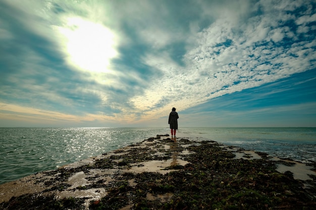 Hermosa foto de una persona caminando sobre una tierra dentro del océano bajo el cielo nublado