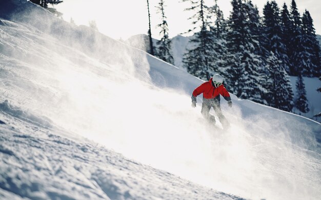 Hermosa foto de una persona con chaqueta roja esquiando por la montaña nevada con fondo borroso