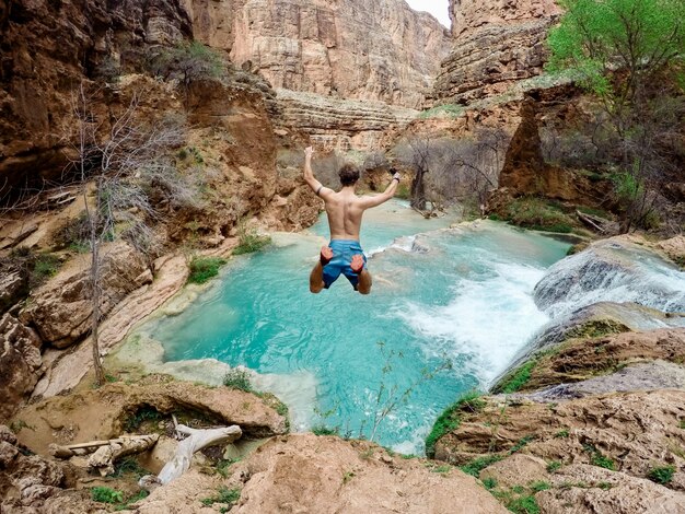 Hermosa foto de una persona con traje de baño saltando desde un acantilado en el agua rodeada de árboles