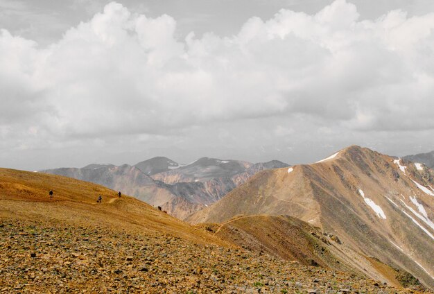 Hermosa foto de personas caminando por la montaña en la distancia bajo un cielo nublado