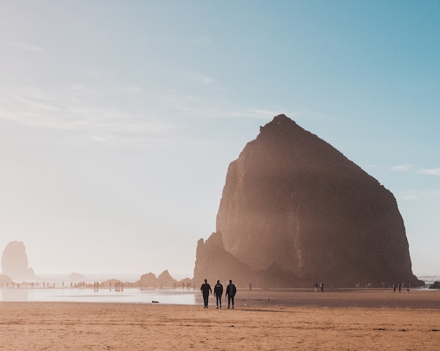 Hermosa foto de personas caminando en la orilla de la playa con una roca en la distancia durante el día