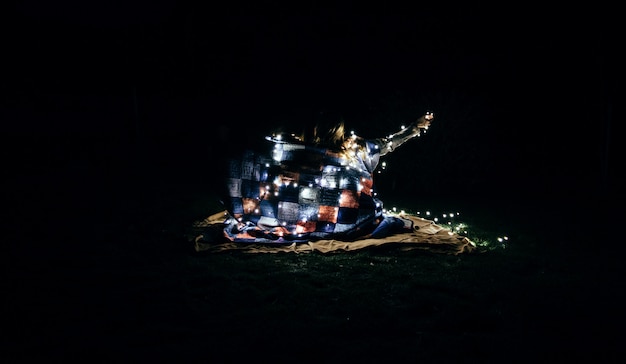 Hermosa foto de personas envueltas en una manta y luces de hadas blancas en la oscuridad