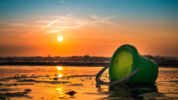 Hermosa foto de la puesta de sol con un cubo verde en la orilla del mar