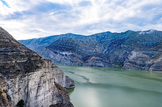 Hermosa foto de un río verde cerca de formaciones de piedra con textura bajo un cielo azul nublado