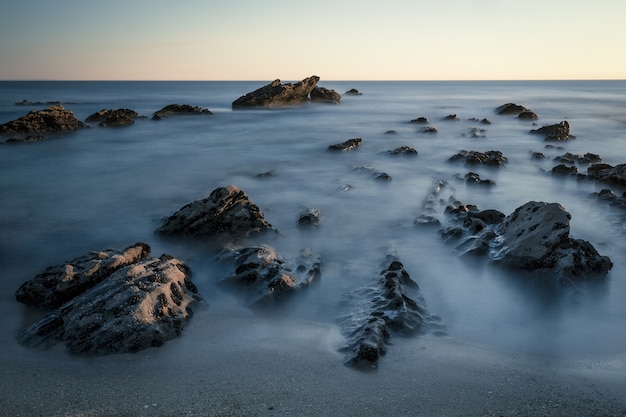 Hermosa foto de rocas en la orilla del mar con un cielo blanco de fondo