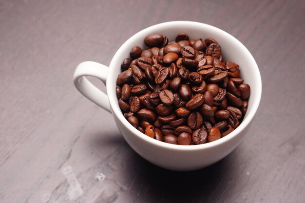 Hermosa foto de taza blanca llena de granos de café en una mesa de madera