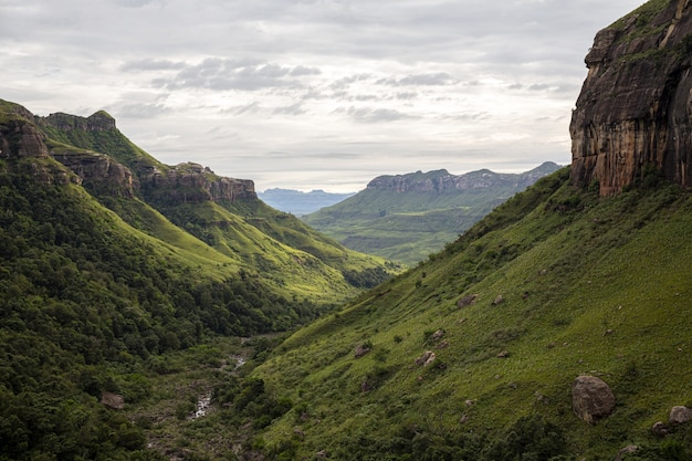 Hermosa foto de un valle verde con rocas altas y colinas empinadas bajo un cielo sombrío gris nublado