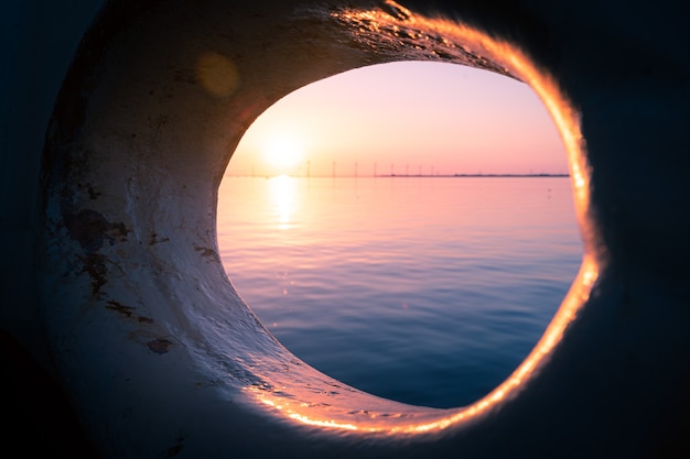 Hermosa foto de la vista de una puesta de sol en el mar visible a través de un agujero redondo en un barco