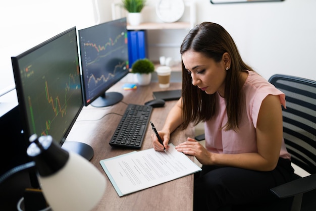 Hermosa freelancer y corredora de bolsa firmando un negocio en su escritorio. Exitosa empresaria leyendo un contrato de trabajo