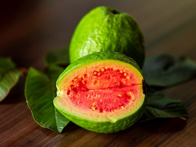 Primer plano de guayaba roja en rodajas con hojas verdes en la mesa de