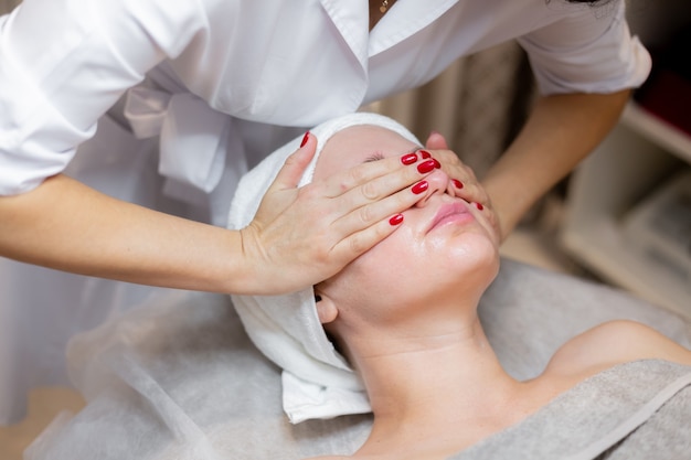 Una hermosa joven se acuesta en la mesa de la esteticista y recibe procedimientos, un ligero masaje facial con aceite.