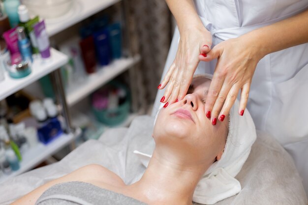 Una hermosa joven se acuesta en la mesa de la esteticista y recibe procedimientos, un ligero masaje facial con aceite.