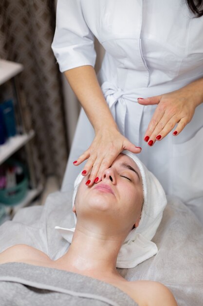 Una hermosa joven se acuesta en la mesa de la esteticista y recibe procedimientos, un ligero masaje facial con aceite.